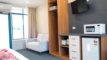 A hotel room with a bed, a seating area with a chair, a wardrobe, a microwave, and a television.