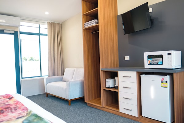A hotel room with a bed, a seating area with a chair, a wardrobe, a microwave, and a television.