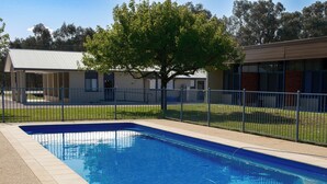 A rectangular swimming pool with a tiled edge, surrounded by a fence and a grassy area. - Holbrook Motel (Holbrook)