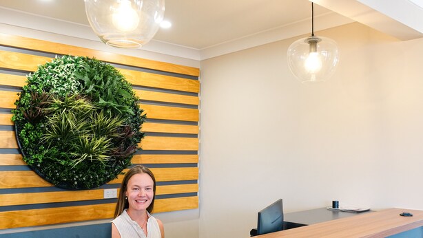 A reception desk with a wooden panel wall, a large green wall-mounted plant, and a modern pendant light. - Holbrook Motel (Holbrook)