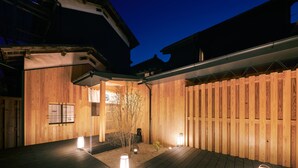 A wooden deck with a small garden area, a wooden fence, and a building with a sloped roof. - Machi-jyu  (Chichibu)