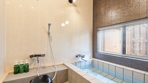 A modern bathroom with a glass-enclosed shower, a vanity with a mirror, and a window with blinds. - Machi-jyu  (Chichibu)
