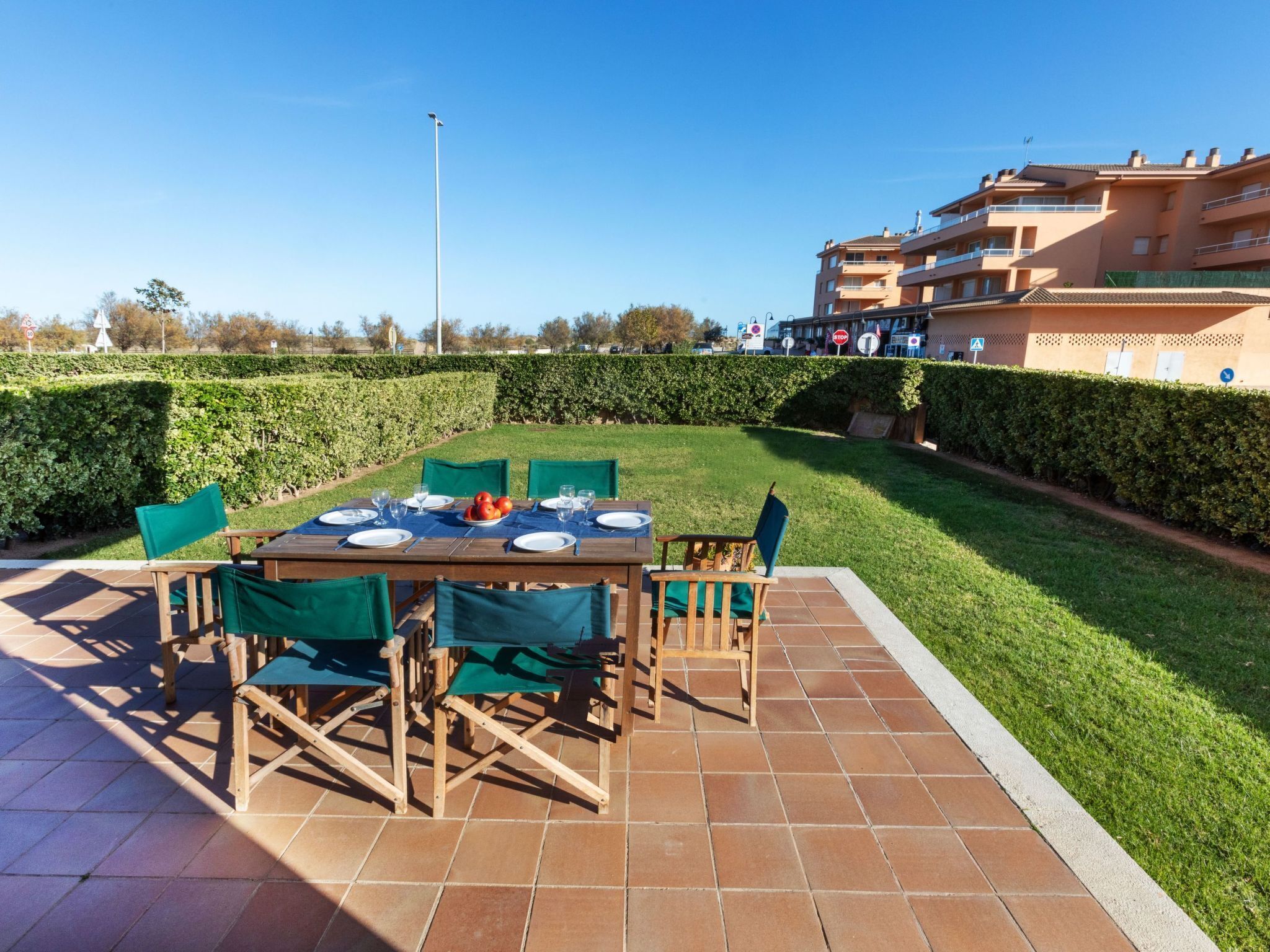 Un área de comedor al aire libre con una mesa de madera dispuesta para cuatro personas, rodeada de sillas verdes.