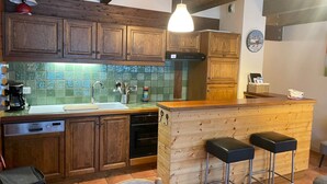Eine Küche mit Holzschränken, einer grünen Fliesenrückwand, einer Kaffeemaschine, einer Spüle, einem Geschirrspüler und einer Holzinsel mit zwei Hockern.