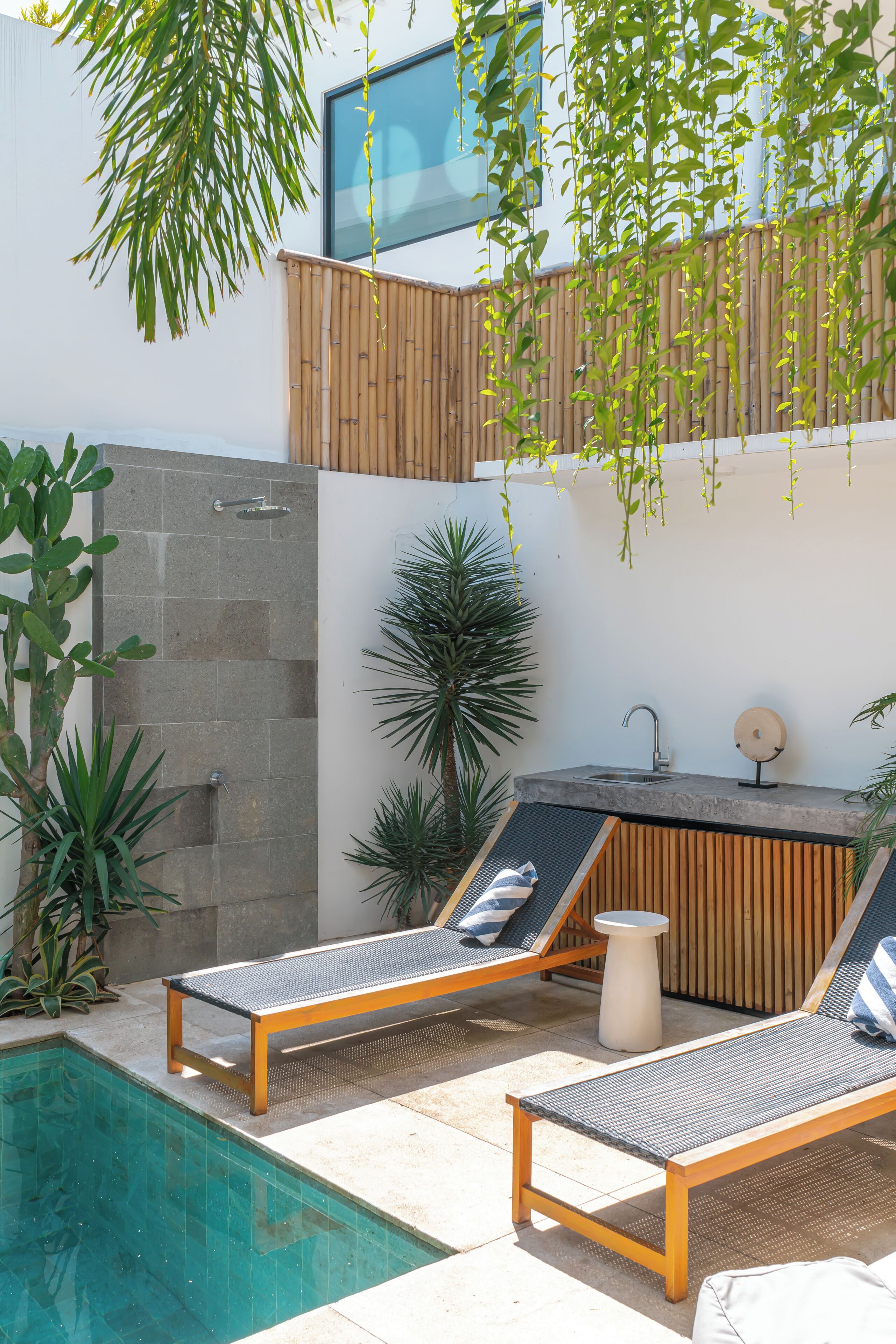 A modern outdoor pool area with two lounge chairs, a small bar, and a stone shower enclosure.