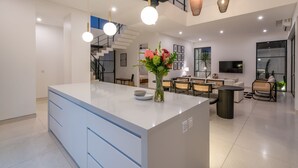 Une cuisine moderne dotée d’un îlot central, d’un coin repas avec télévision et d’un escalier menant à un niveau supérieur.