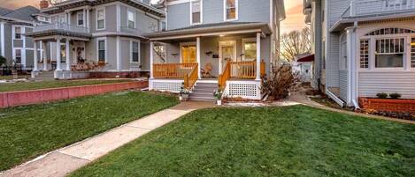 A two-story residential house with a front porch, a small front yard, and a driveway.