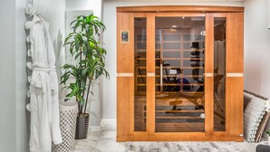 A wooden sliding door with a glass panel, a potted plant, and a white robe hanging on a rack. - Serenity Sauna Retreat - Blocks from Downtown (Sioux Falls)