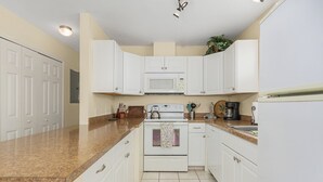Una cocina con gabinetes blancos, microondas, estufa y cafetera.
