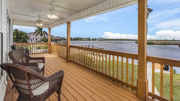 Una terraza de madera con sillas de mimbre, barandilla y vista al río.