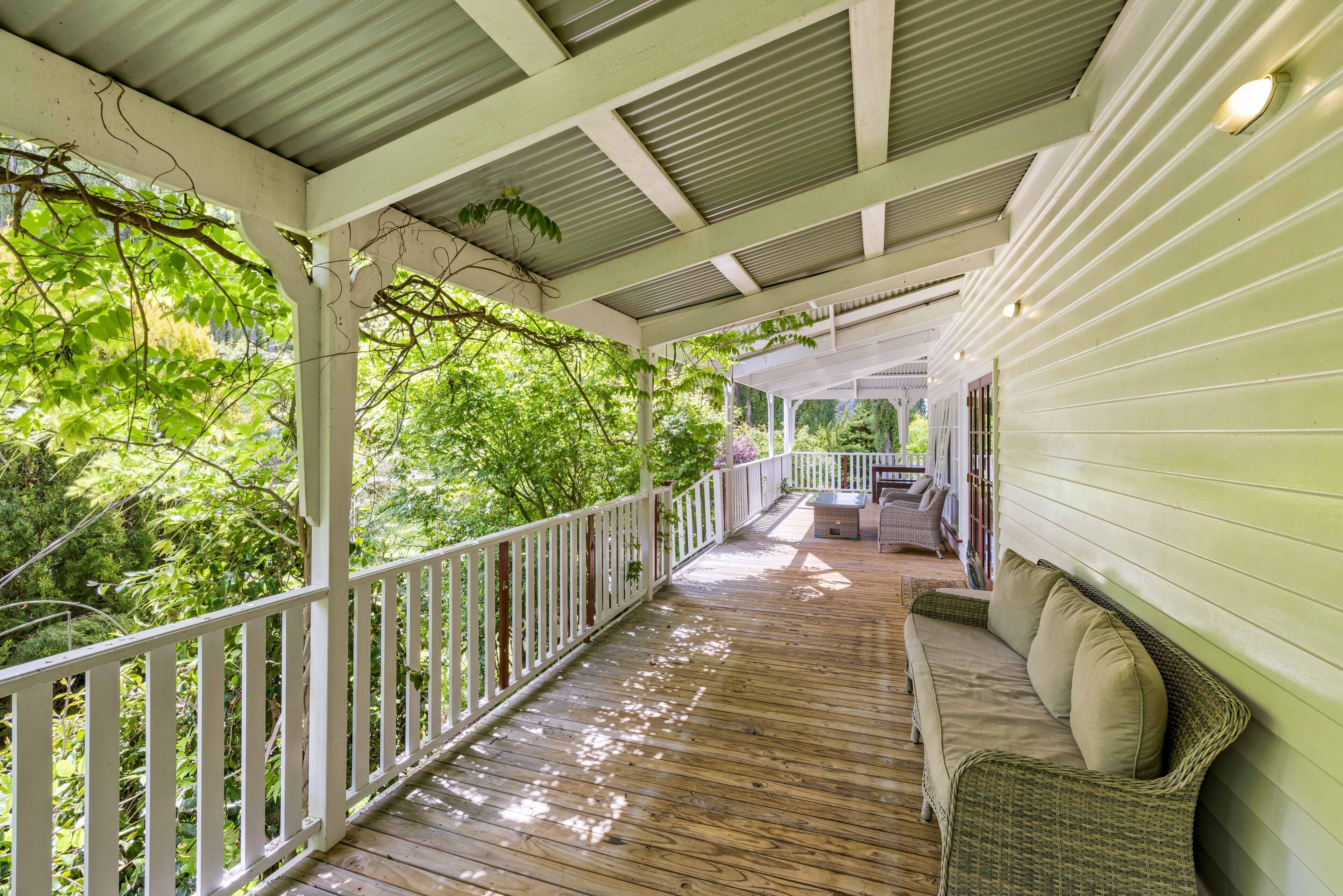 A covered wooden deck with a white railing, a wicker sofa, and a small table.
