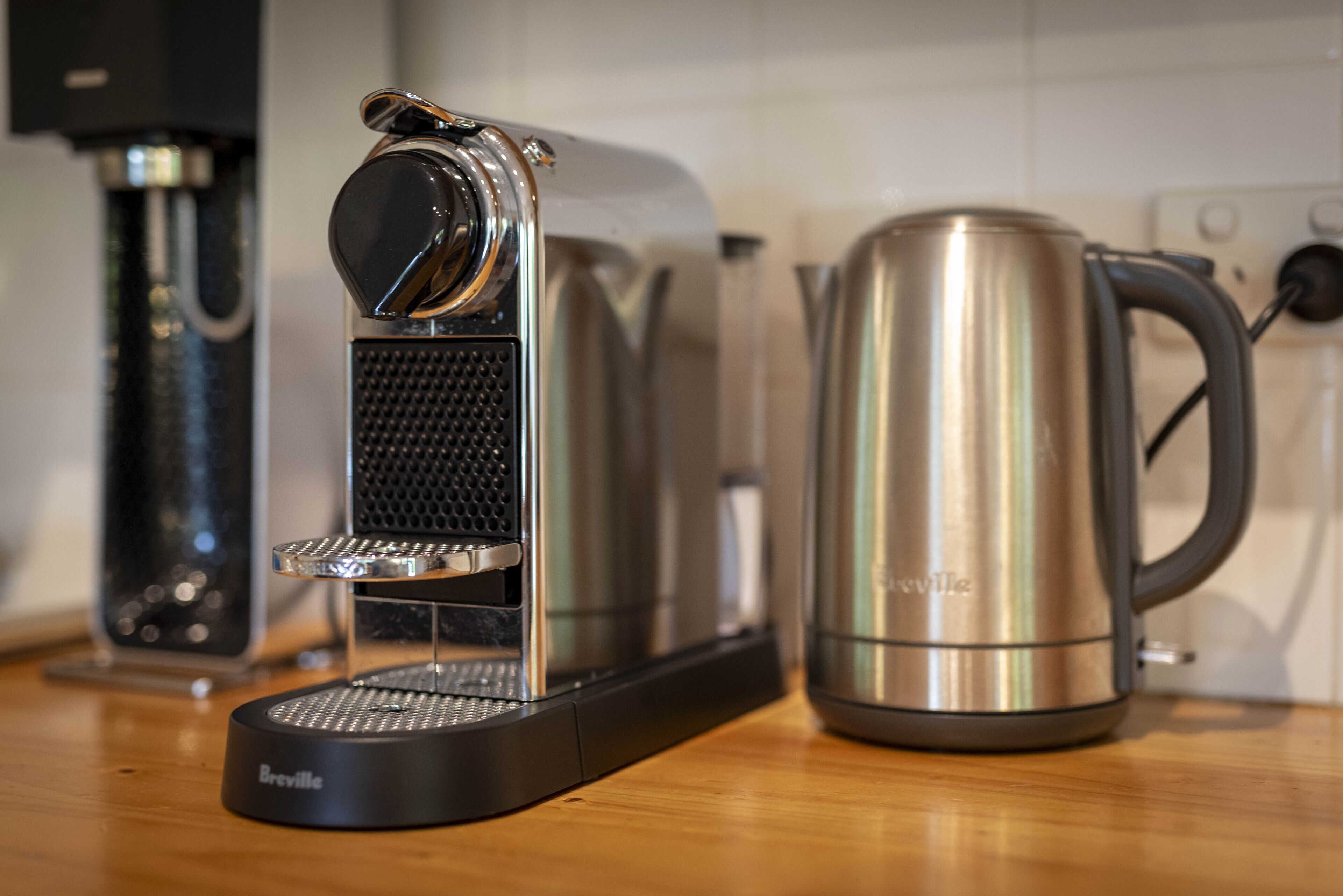 A Breville coffee maker and a stainless steel coffee pot on a wooden countertop.