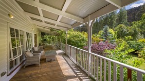Un portico riparato con mobili in vimini, un patio in legno e vista su un rigoglioso giardino e bosco.