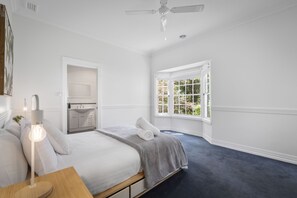 Relax in this serene bedroom with a large bed and ceiling fan, offering a peaceful view of lush greenery.