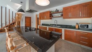 A modern kitchen with a central island, wooden cabinets, and a black countertop. - Villa Lisy  (Canggu)