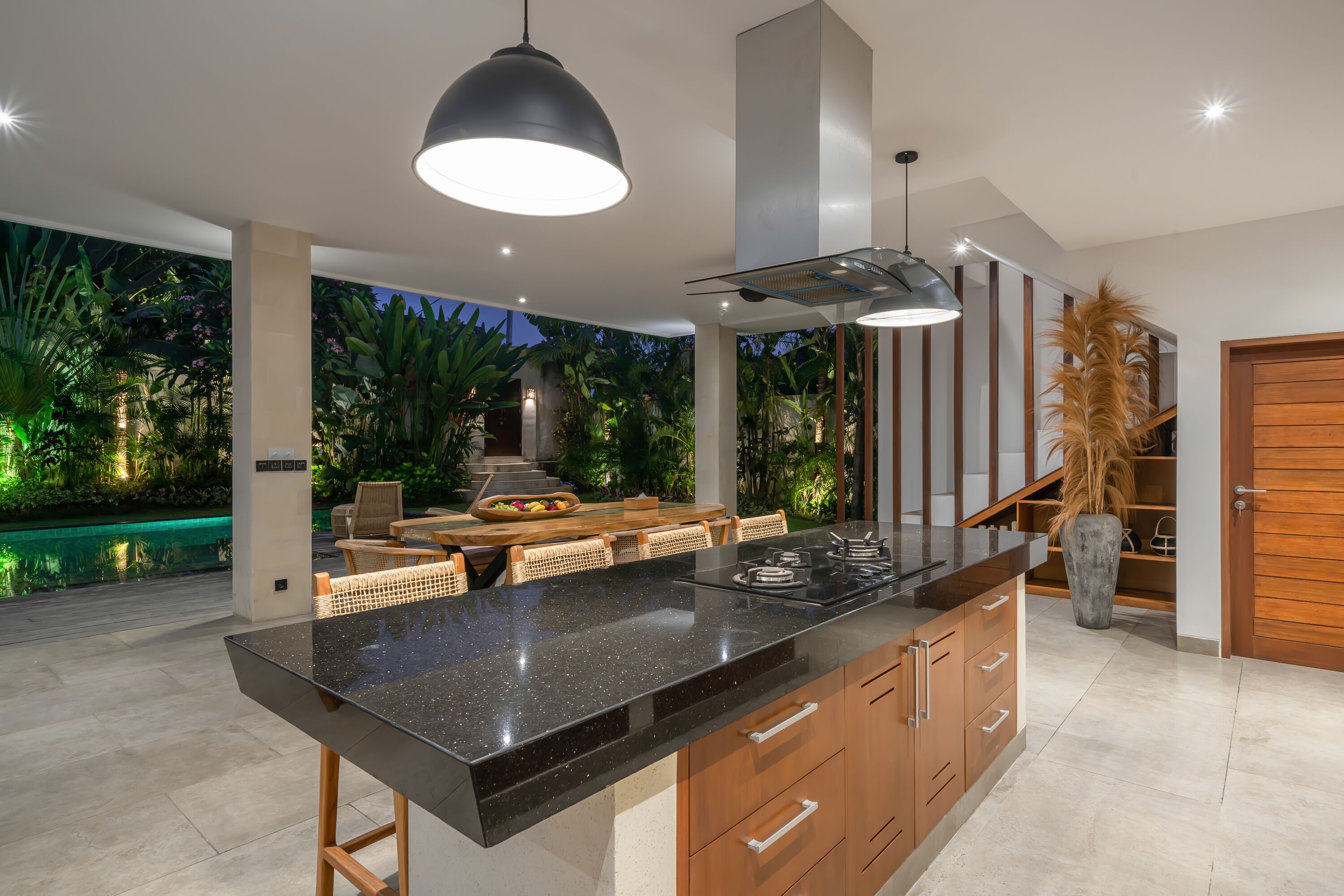 A modern kitchen with a large island, wooden cabinets, and a dining area with outdoor seating.