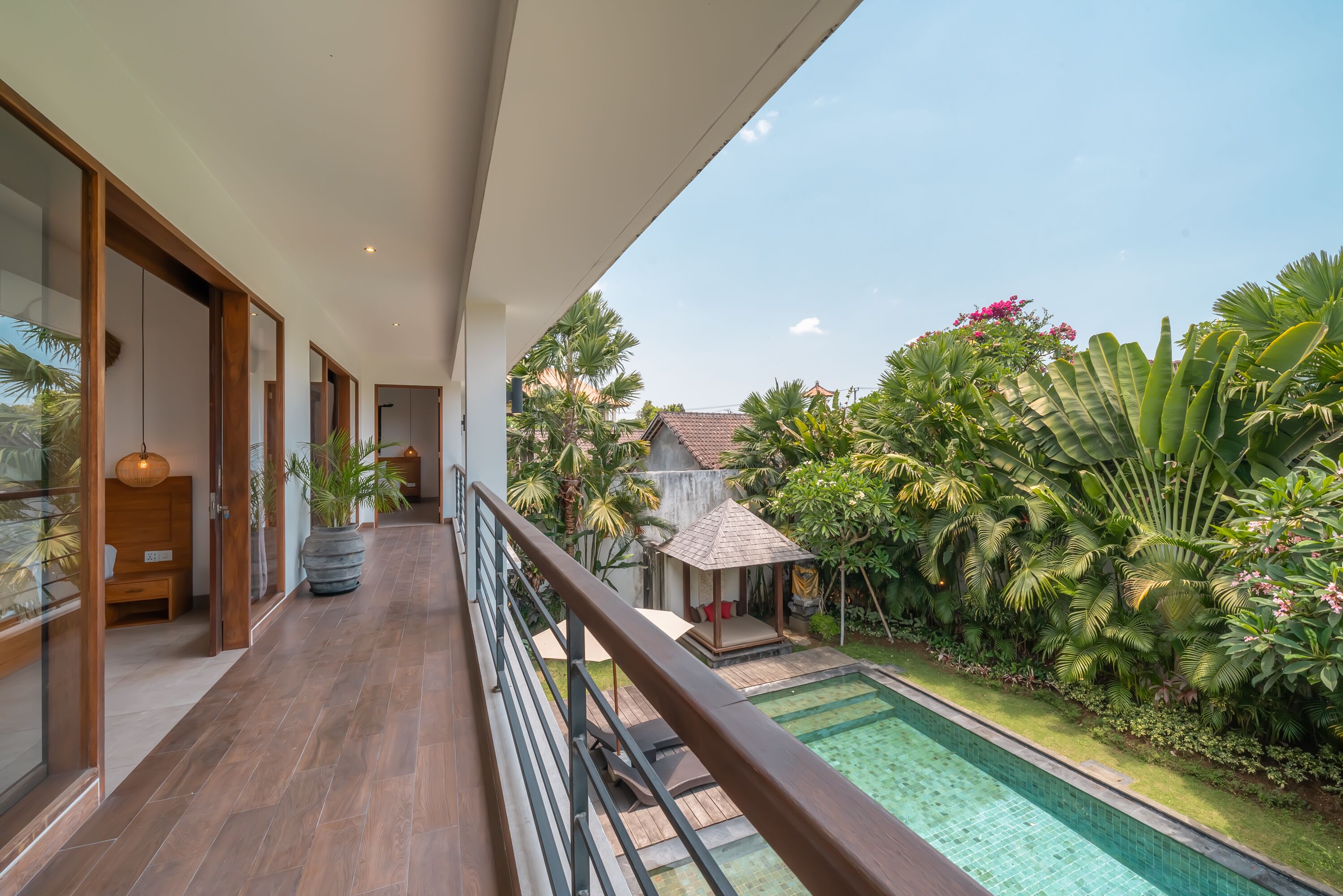 A modern outdoor balcony with a wooden floor, a pool, and lush tropical plants.