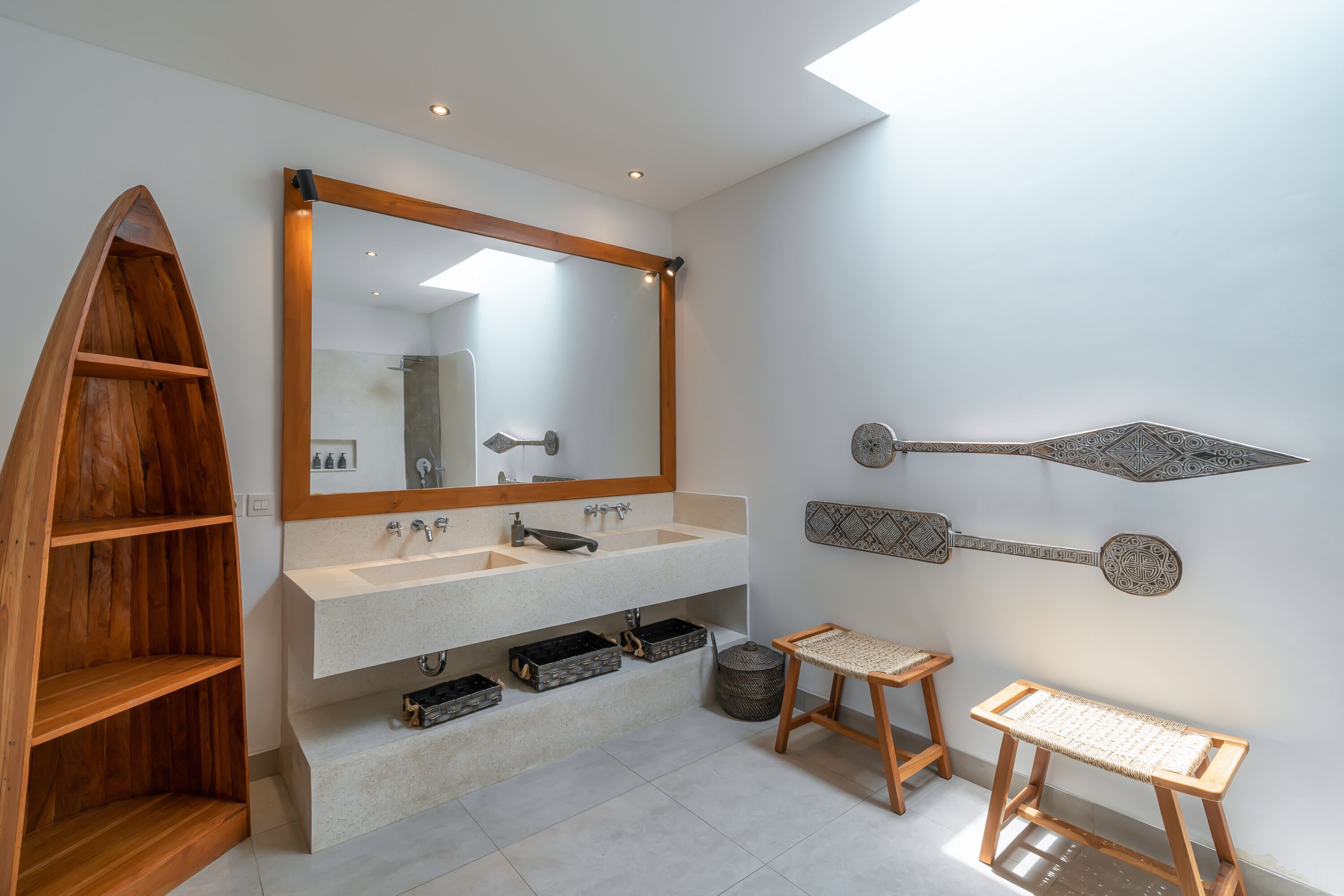 A modern bathroom with a large mirror, two sinks, wooden shelves, and decorative wall art.