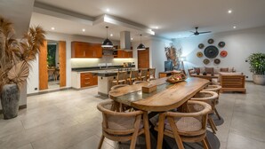 A modern kitchen with wooden cabinets, a central island, and a dining area with wicker chairs. - Villa Lisy  (Canggu)