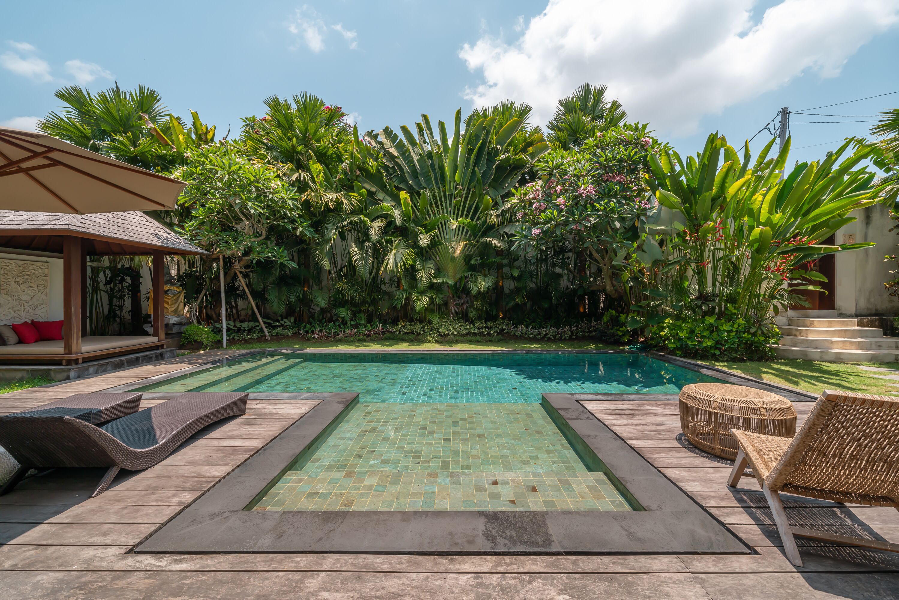 A swimming pool with lounge chairs and a small hot tub, surrounded by lush tropical plants.