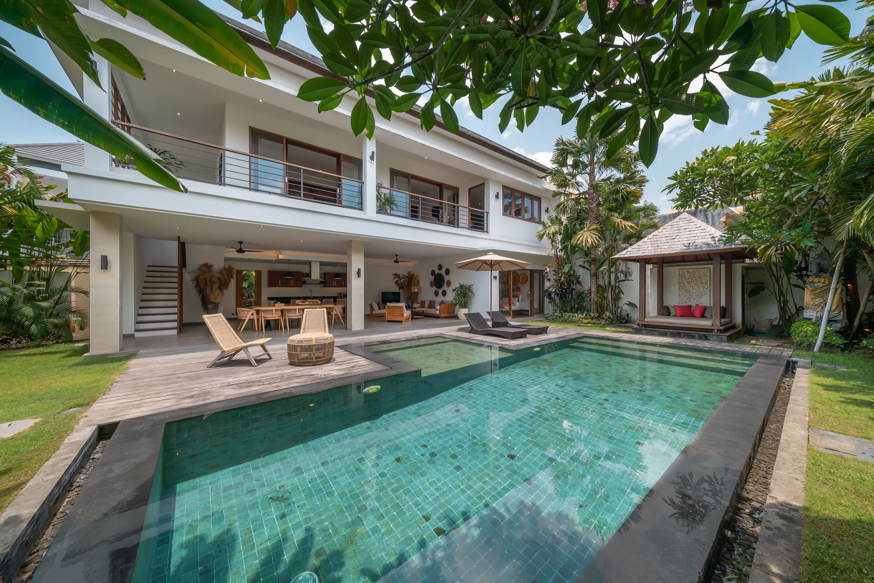 A modern two-story house with a swimming pool, outdoor furniture, and lush greenery.