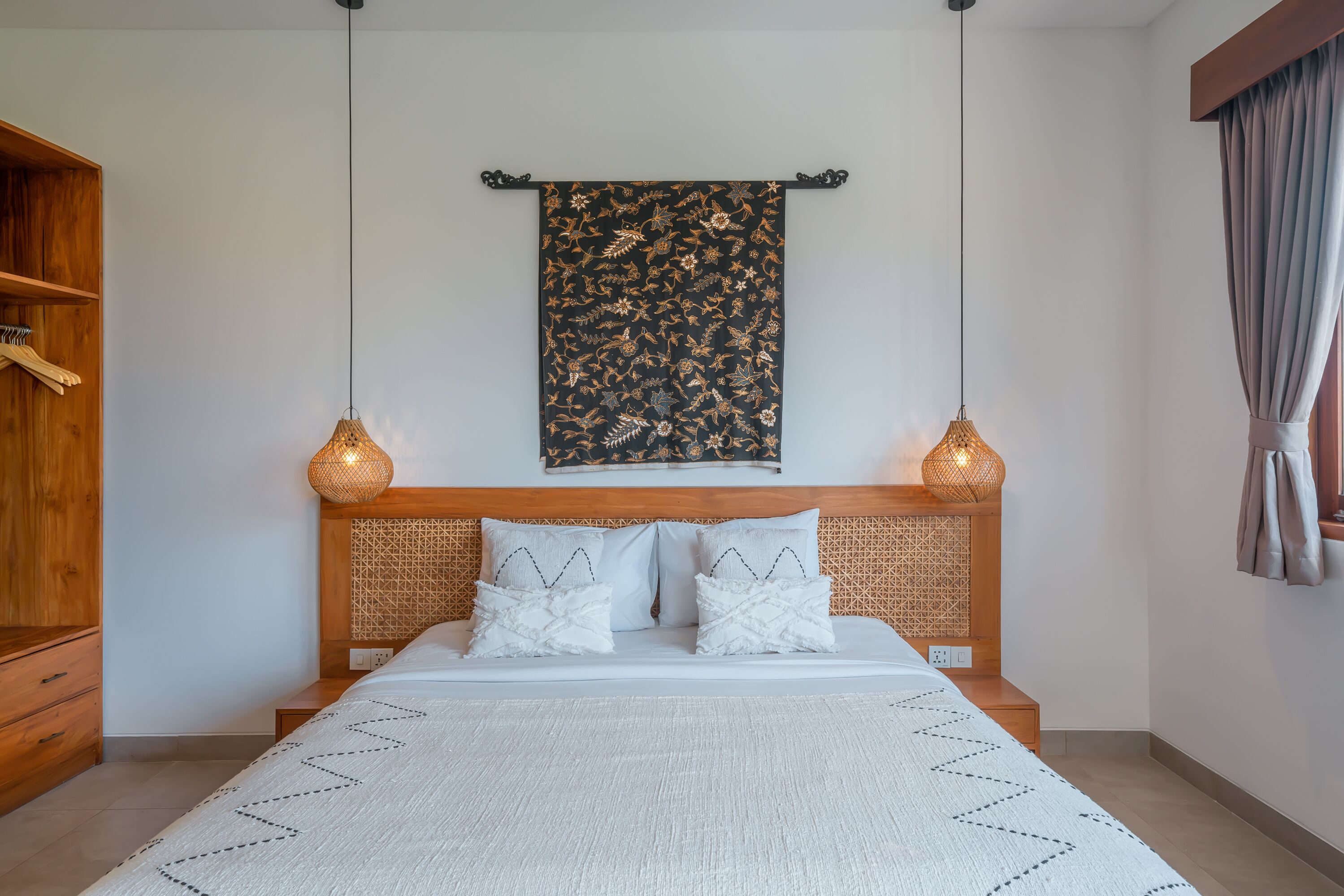 A neatly made bed with a patterned headboard, two bedside lamps, and a hanging tapestry.