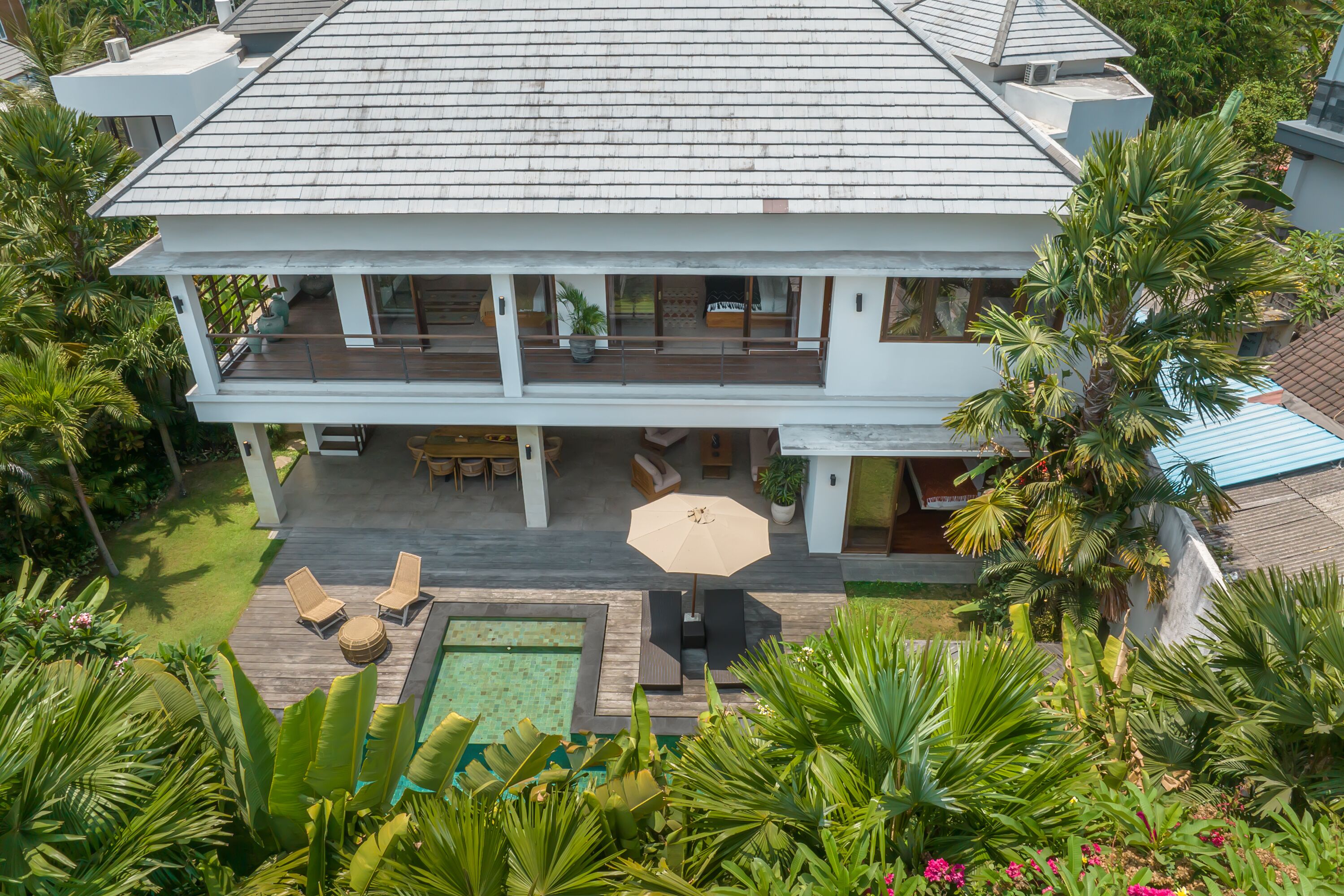 A two-story house with a swimming pool, outdoor seating, and lush greenery.