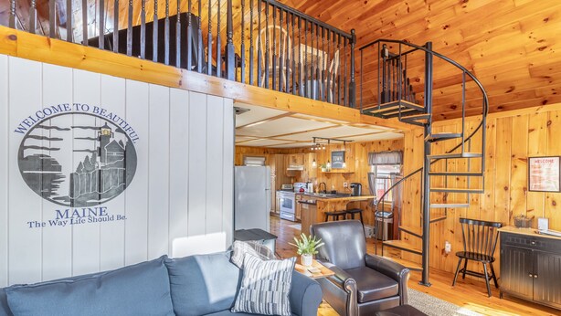 Ein gemütliches Blockhaus-Interieur mit einem blauen Sofa, einem Essbereich, einer Küche und einer Wendeltreppe.