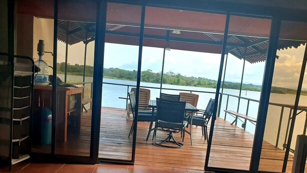 Ein Zimmer mit einem Bett, einem kleinen Tisch und einem Sessel. Blick auf ein Gewässer und grüne Landschaft.