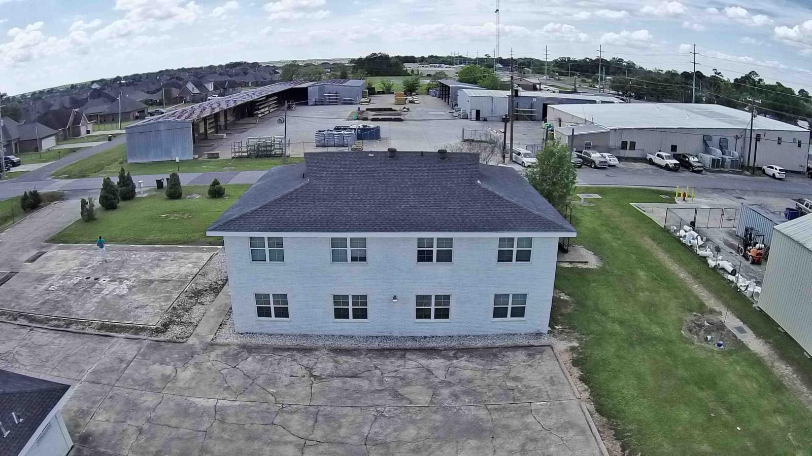 A large industrial building with a flat roof, surrounded by smaller structures and a parking area.