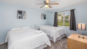 Une chambre avec deux lits, un ventilateur de plafond, une fenêtre avec des rideaux et une table de chevet avec une lampe.