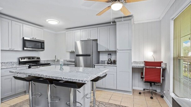 Une cuisine dotée d’un îlot central, d’appareils électroménagers en acier inoxydable et d’un ventilateur de plafond.