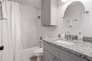 A bathroom with a shower, toilet, sink, and a mirror.