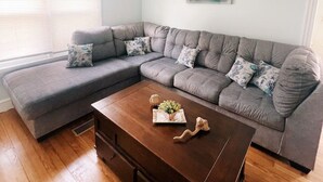 Ein Wohnzimmer mit einem grauen Ecksofa, einem Holztisch und einem an der Wand hängenden abstrakten Gemälde.