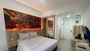A modern hotel room with a large bed, a wooden headboard, a large abstract painting, a mirror, a desk with a coffee maker, and a TV. - Praya Room (South Tangerang)