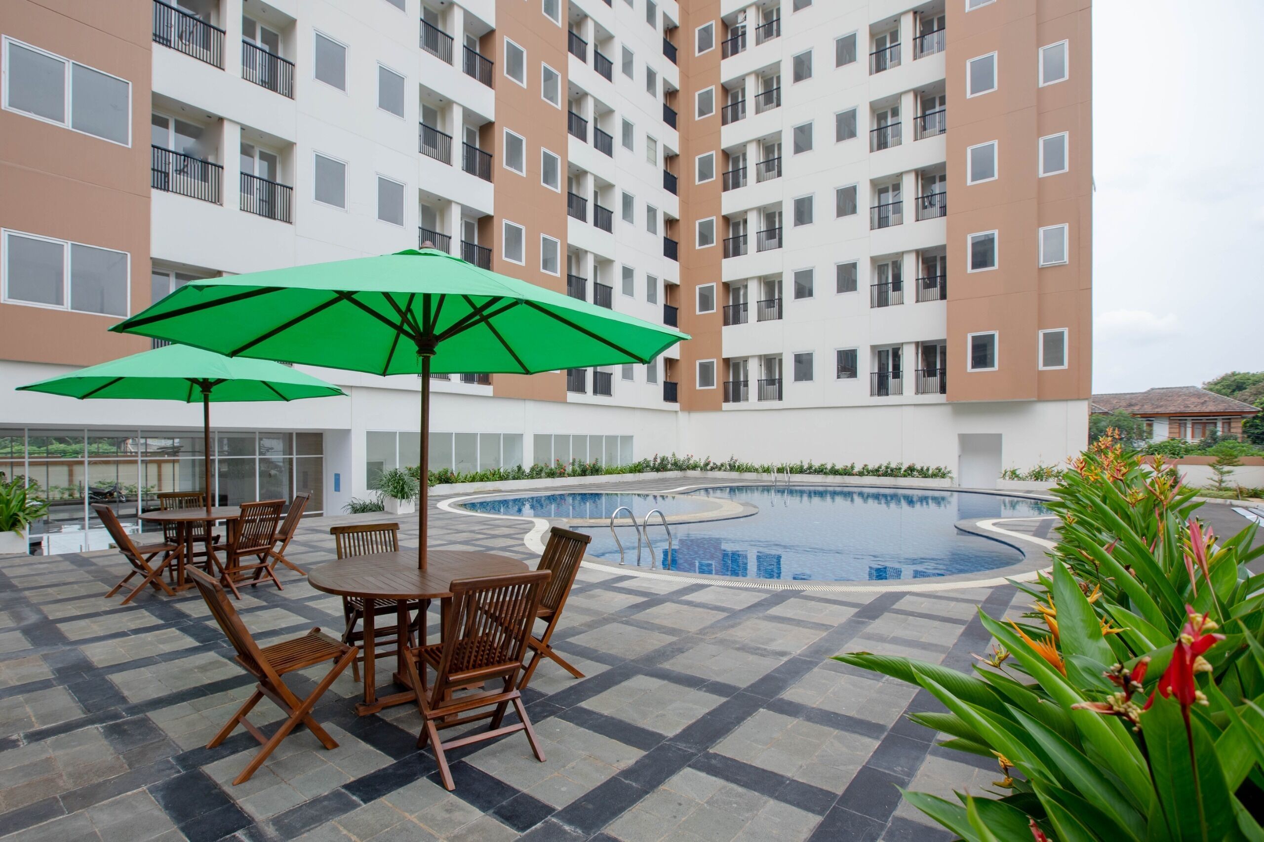 A pool area with a tiled floor, a pool, and a table with chairs and a green umbrella.