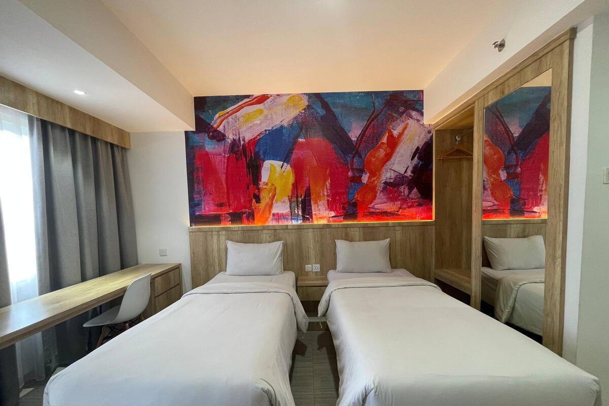 A hotel room with two single beds, a desk, and a large abstract painting on the wall.