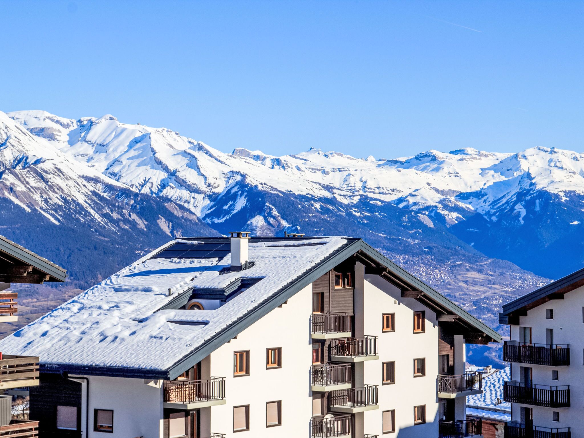 A building with a sloped roof, multiple balconies, and a view of snow-covered mountains.