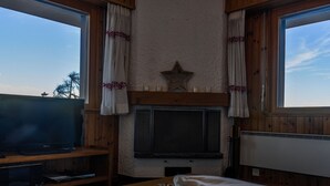 Ein gemütliches Zimmer mit einem HolztV-Schrank, einem Kamin und einem Fenster mit Vorhängen.