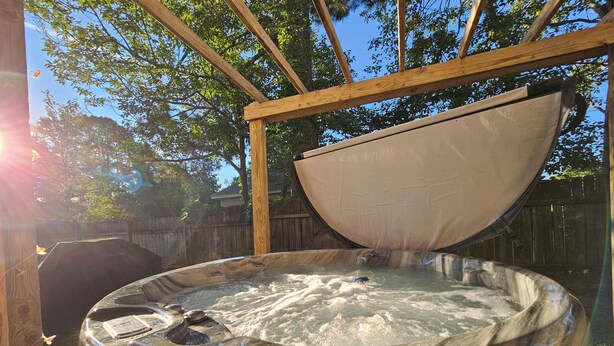 A hot tub with a wooden frame and a cover, surrounded by a wooden fence and trees.
