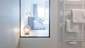 Ein modernes Badezimmer mit weiß gefliesten Wänden, einer gläsernen Duschkabine, einem weißen Handtuchhalter und einem sichtbaren Fenster.