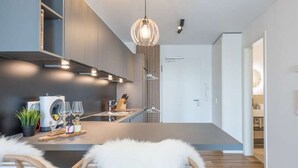 Eine moderne Küche mit einer zentralen Kochinsel, zwei Korbstühlen mit weißen Felldecken und einer Pendelleuchte.