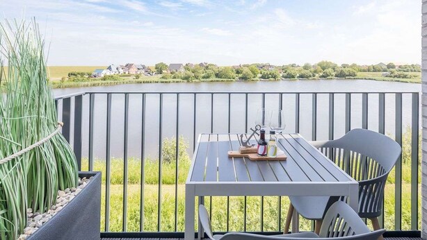 Ein Balkon mit Tisch und Stühlen, der auf ein Gewässer und grüne Vegetation blickt.