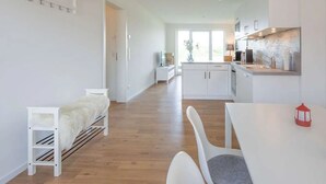 A modern kitchen with white cabinets, a dining area with a white table and chairs, and a small white bench with a fur throw. - Liselotte by Interhome (Nordstrand)