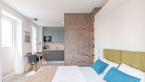 A modern bedroom with a large bed, a desk, and a kitchenette in the background. - Heewer Stuuv by Interhome (Nordstrand)