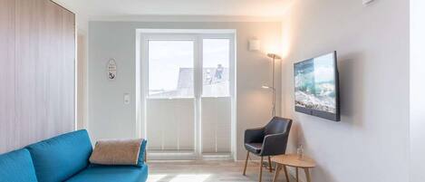 A modern living room with a blue sofa, a small round table, a floor lamp, and a large window with blinds.