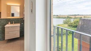 A bathroom with a sink, mirror, and a view of a river and greenery outside. - Heewer Stuuv by Interhome (Nordstrand)