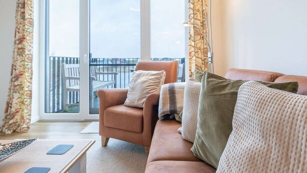Un salon comprenant un canapé, un fauteuil et une lampe sur pied. Il y a un balcon avec une balustrade et une vue sur l’extérieur.