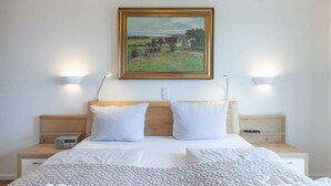 Une chambre d’hôtel comprenant un lit, deux tables de chevet, une commode, un tableau et des lampes fixées au mur.