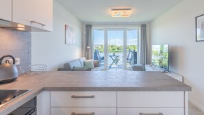 A modern kitchen with a large island, a dining area with a table and chairs, and a view of a lake through large windows. - Die Komfortzone by Interhome (Nordstrand)
